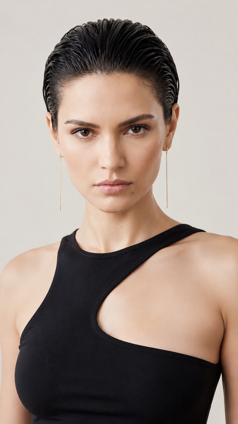 An upper body close-up of a female model with a classic slicked-back wet look pixie hair in jet black. She wears delicate gold thread earrings and an edgy asymmetric black summer tank top. Set against a minimalist soft beige studio background. The model gazes confidently into the camera with a calm expression, captured from a straight-on eye-level angle.